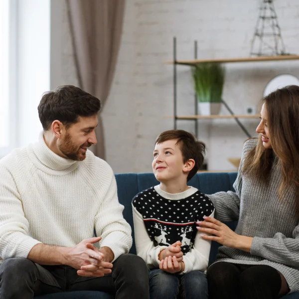 Une famille assise sur un canapé, avec un enfant au centre, souriant et profitant d'un moment ensemble.