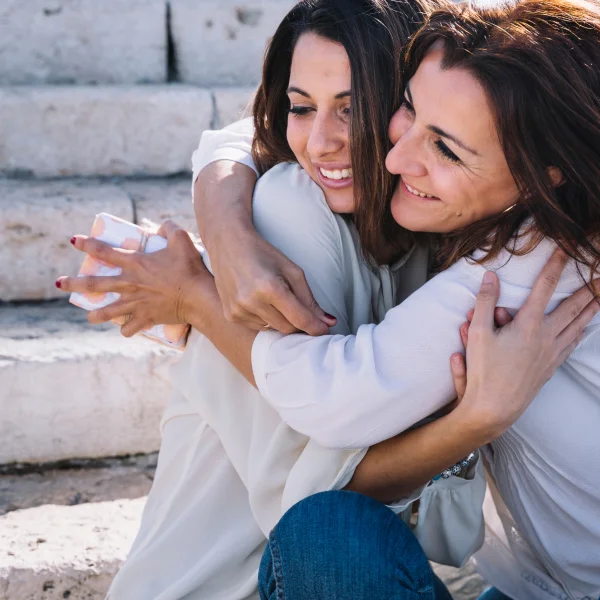 Deux femmes s'enlacent sur des marches, exprimant une forte connexion émotionnelle.
